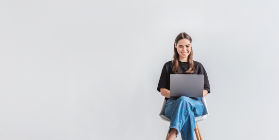 Eine junge Frau sitzt auf einem Stuhl und ließt am Laptop
