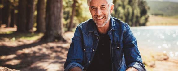 Älterer Mann sitzt im Wald und lacht