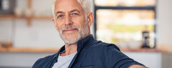 Älterer Mann sitzt lächelnd auf der Couch