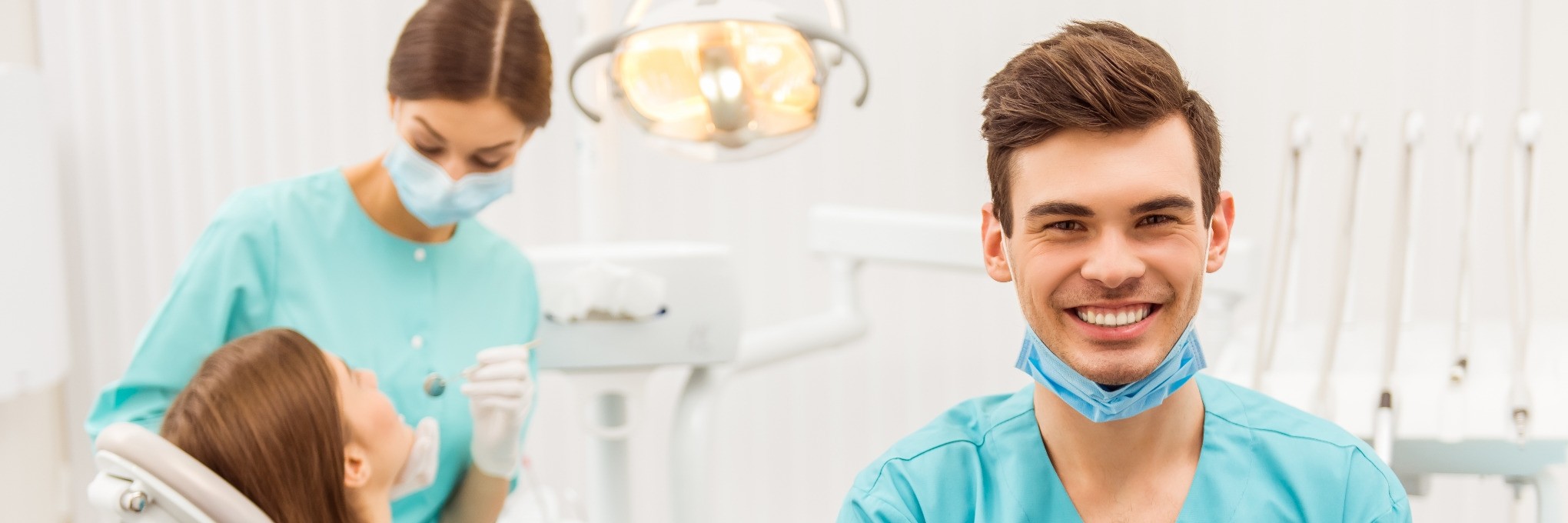 Junger Assistent lacht während im Hintergrund eine Patientin behandelt wird